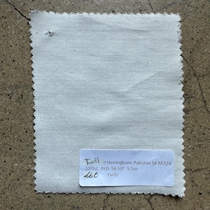 Pode incluir: Uma amostra de tecido branco de sarja de espinha de peixe com o texto "Twill Herringbone Pakistan S# RA324 100%C PFD 58-59" 5,5 oz 660 Jardas".