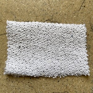 May include: A white, textured, rectangular fabric with a slightly frayed edge.