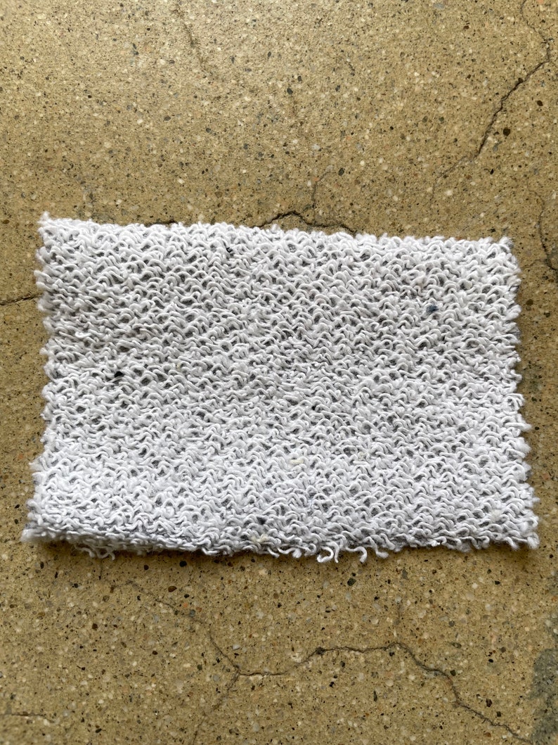 May include: A white, textured, rectangular fabric with a slightly frayed edge.