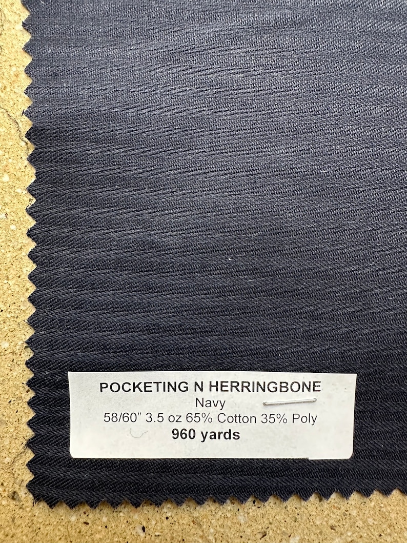 Pu&ograve; includere: Campione di tessuto blu navy con trama a spina di pesce. L'etichetta riporta "POCKETING N HERRINGBONE Navy 58/60" 3.5 oz 65% Cotone 35% Poli 960 yards".