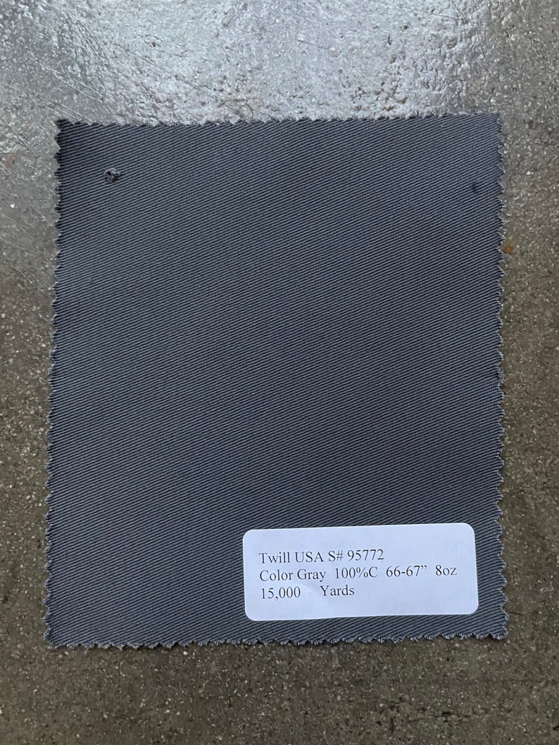以下が含まれることがあります： グレーのツイル生地見本で、"Twill USA S# 95772 Color Gray 100%C 66-67" 8oz 15,000 Yards"というテキストが書かれています。
