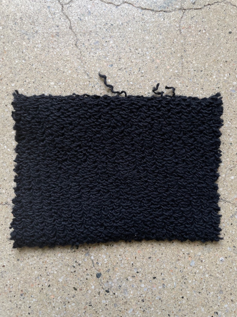 May include: A black, textured fabric swatch with a slightly frayed edge.