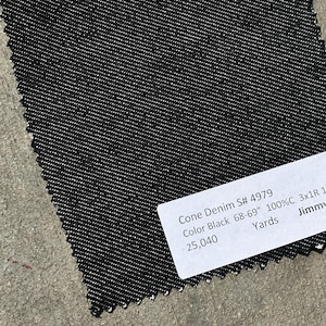 May include: A swatch of black Cone Denim fabric with a textured weave. A white label displays the text "Cone Denim S# 4979 Color Black 68-69" 100%C 3x1R 1". The label also indicates the quantity of fabric in yards.
