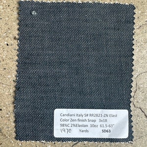 May include: A dark blue denim fabric swatch with a white label that reads "Candiani Italy S# RR2821-ZN Elast Color Zen finish Snap 3x1R 98%C 2% Elastan 10oz 61.5-63" 1970 Yards SD63"