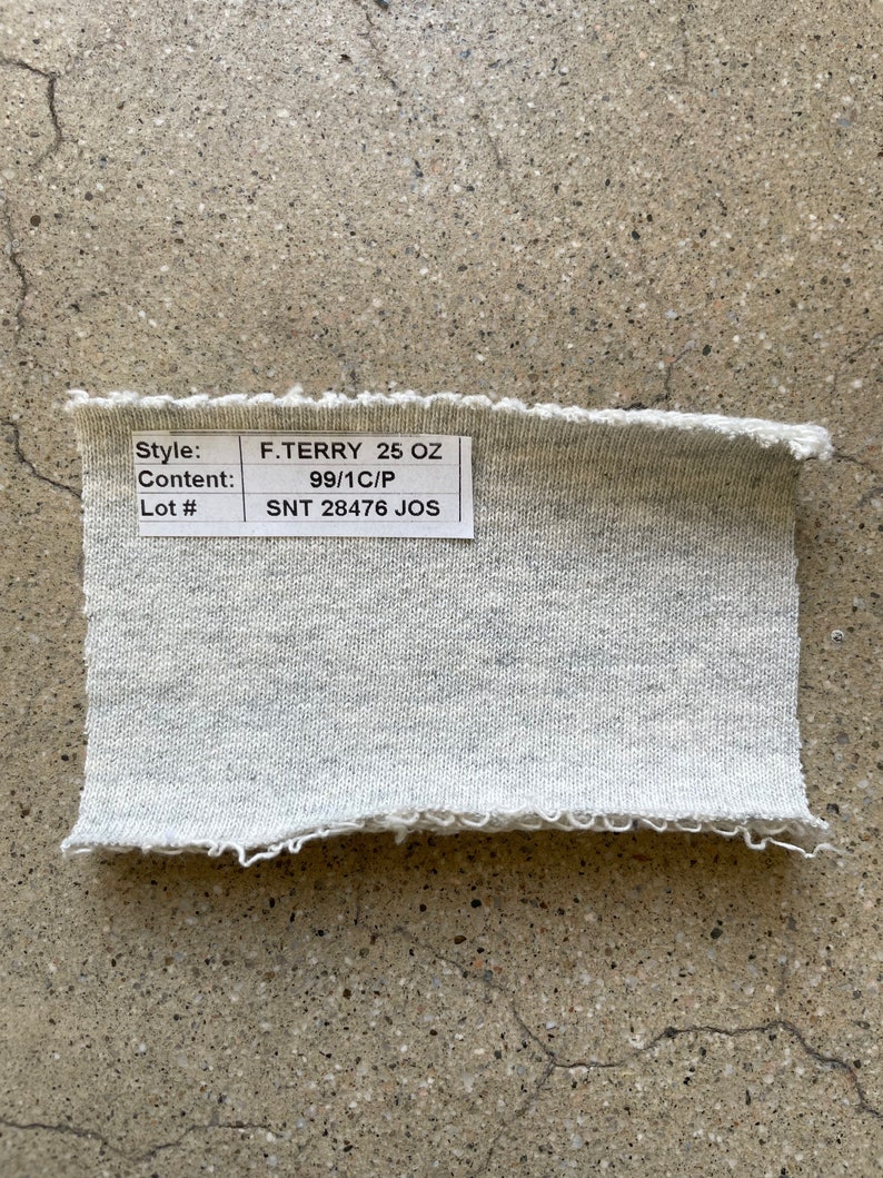 May include: A close-up of a gray fabric swatch with a white label that reads "Style: F.TERRY 25 OZ", "Content: 99/1C/P", and "Lot #: SNT 28476 JOS".