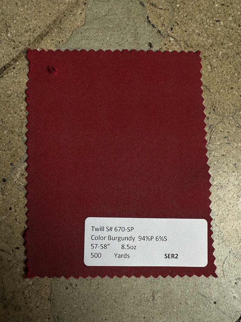 May include: A burgundy twill fabric swatch with a white label that reads 'Twill S# 670-SP', 'Color Burgundy 94%P 6%S', '57-58' 8.5oz', '500 Yards', and 'SER2'.