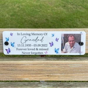 May include: White memorial plaque with a photo of a man and the text "In Loving Memory Of Grandad 13.11.1935 - 03.09.2022 Forever loved & missed Never forgotten" with blue butterfly graphics.