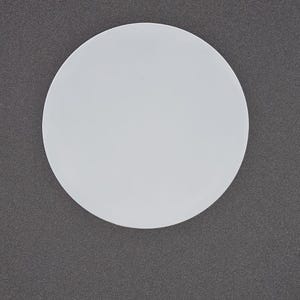 May include: A plain, white, circular object against a dark grey background. The object is a perfect circle, and the lighting creates a subtle gradient across its surface. The background has a textured appearance.