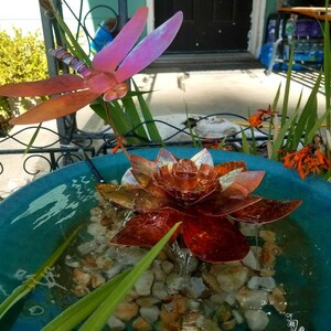 May include: A copper-colored metal lotus flower fountain with a dragonfly sculpture above it. The fountain is in a blue ceramic bowl with water and rocks.