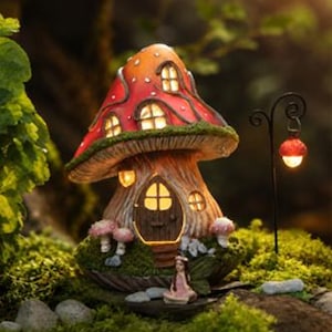 May include: A mushroom-shaped house with a red and orange cap featuring white spots and illuminated windows. The base resembles a tree trunk with a dark brown door and small pink mushrooms. A small figure sits in front, next to a black metal lamp post.