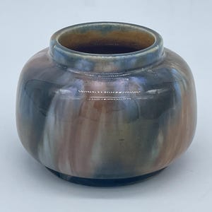 Peut inclure: Un petit vase rond en céramique avec un glaçage brun, bleu et blanc. Le vase a un bord légèrement évasé et une base arrondie.