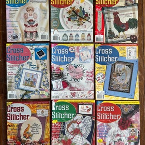 May include: A collection of nine Cross Stitcher magazines arranged in a grid, each featuring colorful embroidery patterns, seasonal themes, and instructional text on the covers, showcasing various cross-stitch projects like angels, roosters, and floral designs.
