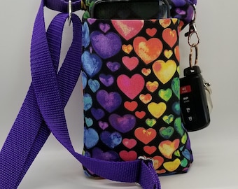 May include: A water bottle holder with a colorful heart pattern, a purple adjustable strap, and a pocket for a phone. The holder has a clip for keys and a water bottle inside.