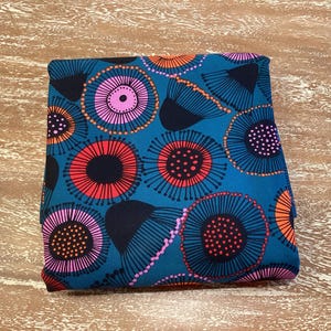 May include: Teal fabric with a repeating pattern of pink, red, black and orange stylised flowers. The flowers have a circular shape with a central circle and radiating lines.