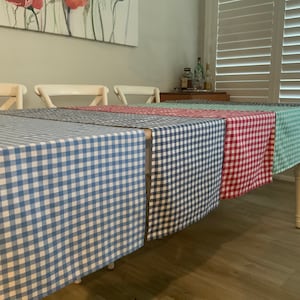 May include: Four checkered table runners in blue, green, red, and white on a white table. The table runners are made of a woven fabric with a gingham pattern.