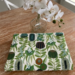 May include: A white tablecloth with a green and brown floral pattern. The pattern features stylised flowers, leaves, and stems. The fabric has a white background with a repeating pattern.