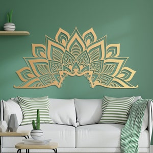 Puede incluir: Una decoraci&oacute;n de pared de mandala dorada y compleja con un dise&ntilde;o floral, colgada sobre un sof&aacute; blanco con almohadas a rayas verdes y blancas en un ambiente de sala de estar.