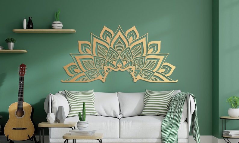 Puede incluir: Una decoraci&oacute;n de pared de mandala dorada y compleja con un dise&ntilde;o floral, colgada sobre un sof&aacute; blanco con almohadas a rayas verdes y blancas en un ambiente de sala de estar.