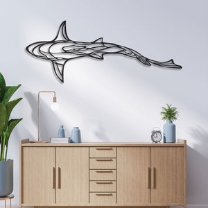 May include: A black metal shark wall art piece. The shark is depicted in a stylized, abstract design, mounted on a white wall. The room features a wooden cabinet, a potted plant, and decorative items.