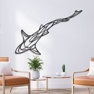 May include: A black metal shark wall art piece. The artwork is mounted on a white wall, with a modern design. The shark is depicted in a stylized, abstract form. The room features two chairs, a small table, and a plant.