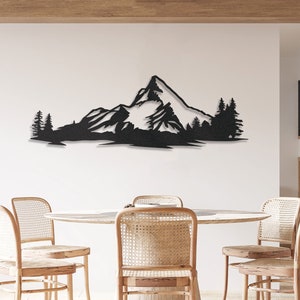 May include: Black metal wall art depicting a mountain range with trees in front of it. The art is mounted on a white wall in a dining room setting.