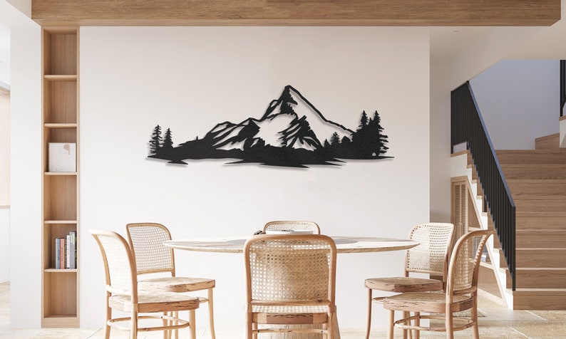 May include: Black metal wall art depicting a mountain range with trees in front of it. The art is mounted on a white wall in a dining room setting.