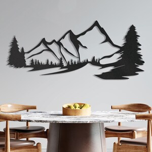 May include: Black metal wall art depicting a mountain range with a river flowing through it. The art piece is mounted on a white wall above a wooden table with chairs.