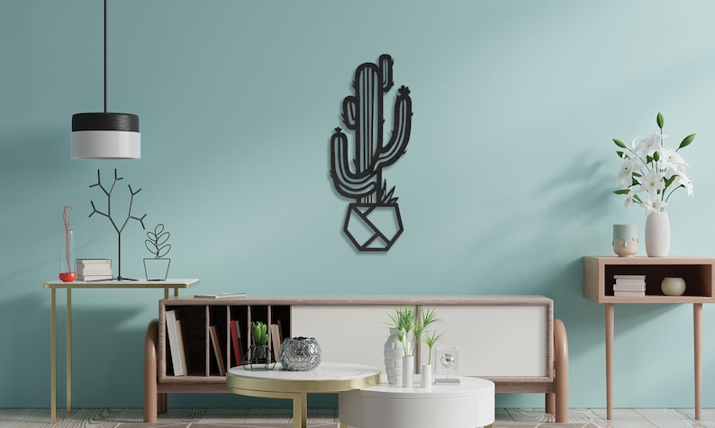 May include: Black metal wall art featuring a cactus in a geometric pot. The art is displayed on a light blue wall in a living room setting.