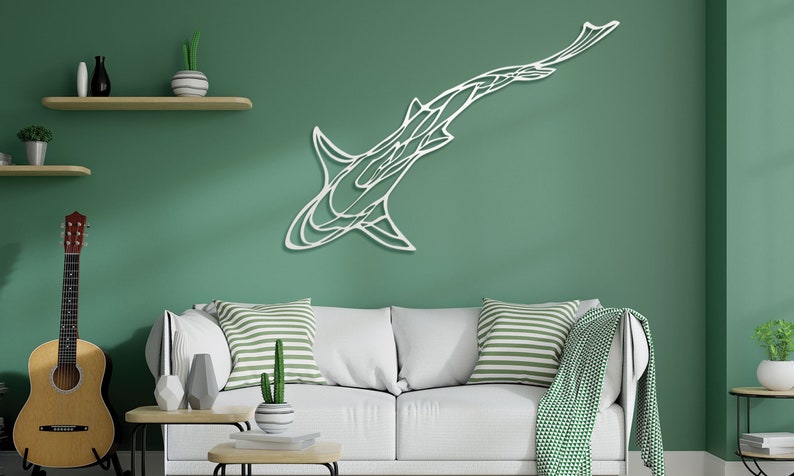 May include: White metal shark wall art. The artwork is mounted on a green wall above a white sofa with striped pillows. A guitar and decorative shelves are also visible in the room.