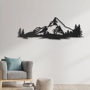 May include: Black metal wall art depicting a mountain range with snow-capped peaks and trees. The art is mounted on a white wall in a living room setting.