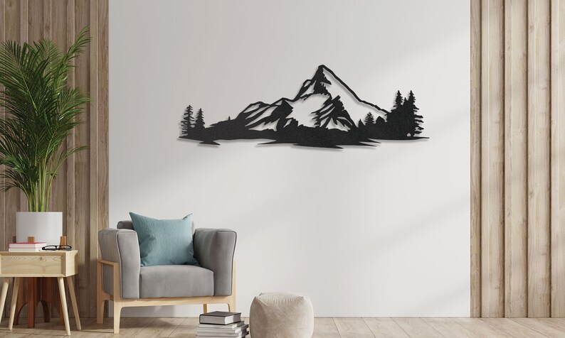 May include: Black metal wall art depicting a mountain range with snow-capped peaks and trees. The art is mounted on a white wall in a living room setting.