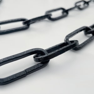 以下が含まれることがあります： 楕円形のリンクでできた黒いチェーンのクローズアップ。チェーンは白い表面の上に置かれています。