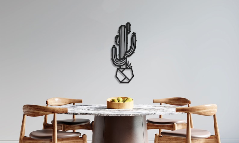 May include: Black metal wall art depicting a stylised cactus in a geometric pot. The art is displayed on a white wall above a wooden table with chairs.