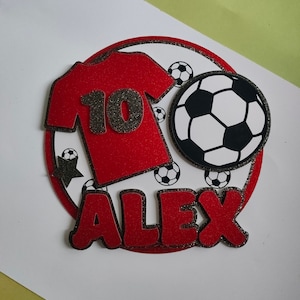 May include: Red and black soccer-themed cake topper with a red jersey with the number 10, a black and white soccer ball, and the name "ALEX" in red letters.
