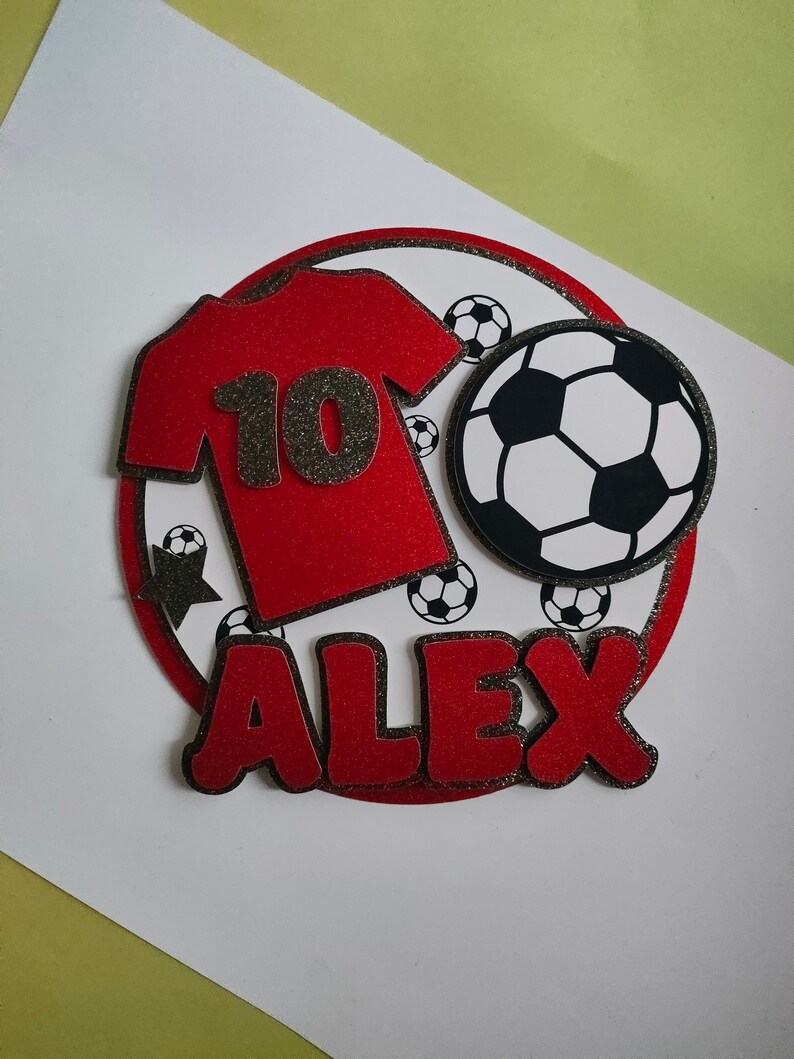 May include: Red and black soccer-themed cake topper with a red jersey with the number 10, a black and white soccer ball, and the name "ALEX" in red letters.