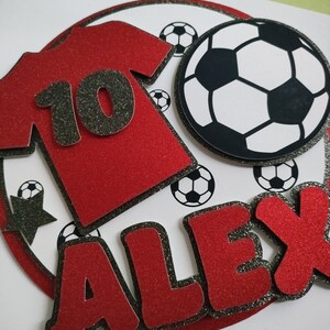 May include: Red and black glitter cake topper with a soccer ball, a red jersey with the number 10, and the name Alex.