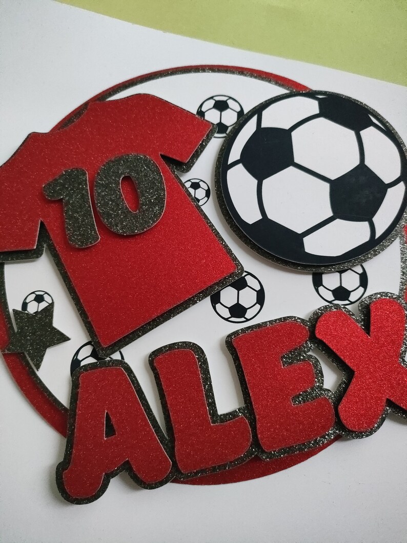 May include: Red and black glitter cake topper with a soccer ball, a red jersey with the number 10, and the name Alex.