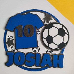 May include: Blue and black soccer-themed cake topper with the name Josiah and the number 10.
