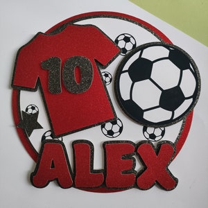 May include: Red and black soccer-themed cake topper with a red jersey with the number 10, a black star, and the name Alex in red letters.