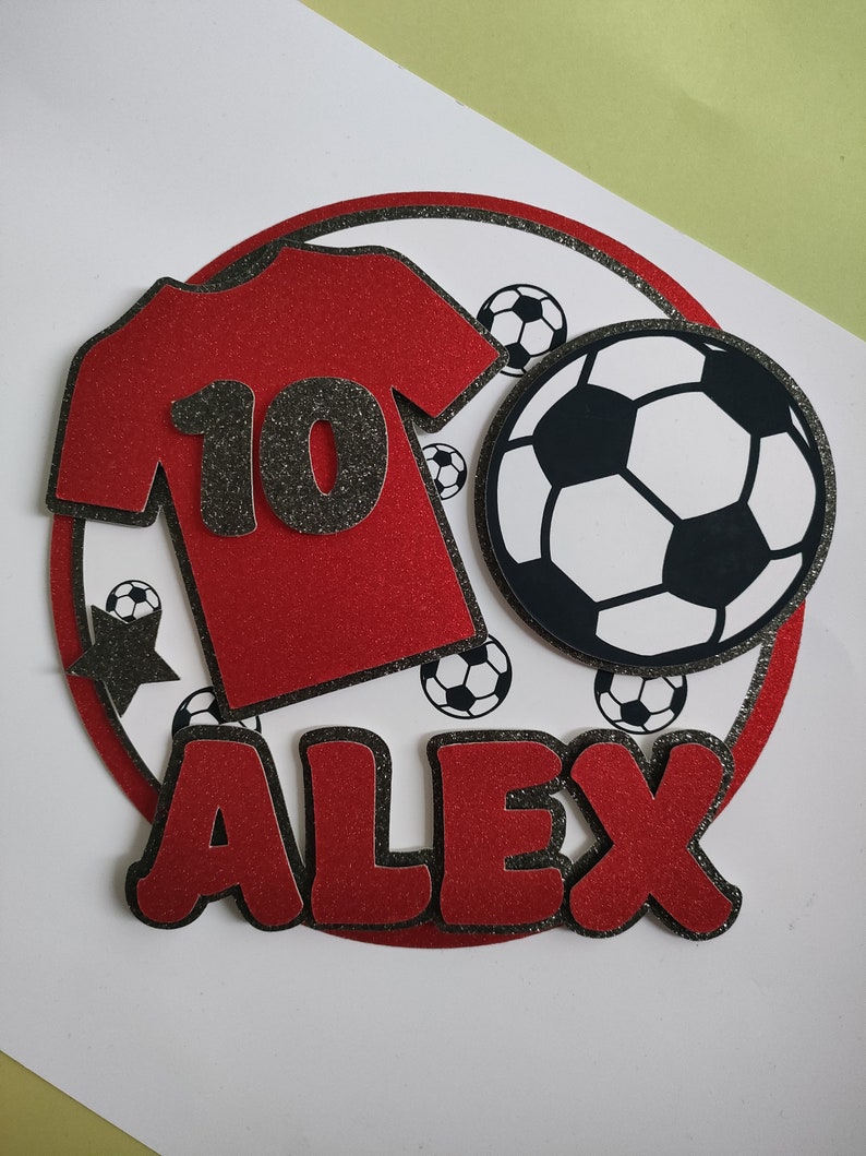 May include: Red and black soccer-themed cake topper with a red jersey with the number 10, a black star, and the name Alex in red letters.