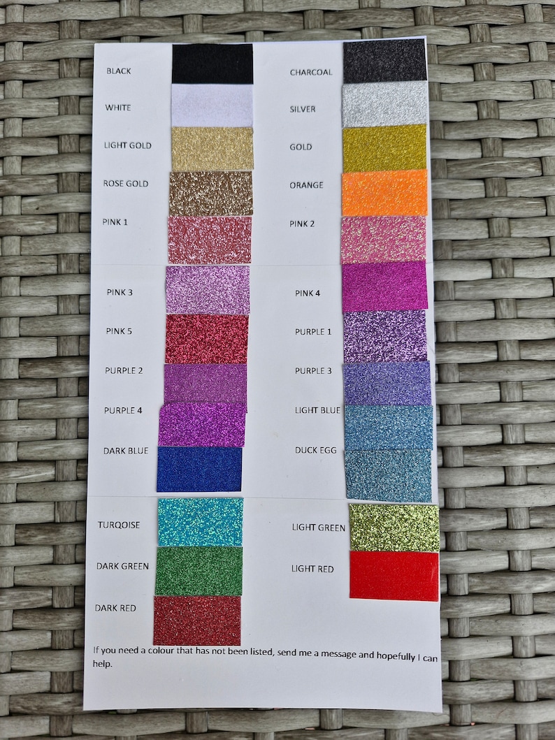 May include: A color chart featuring rectangular swatches of glittery material in various shades including black, white, gold, pink, purple, blue, green, and red. Each swatch is labeled with its corresponding color name in black text on a white background.