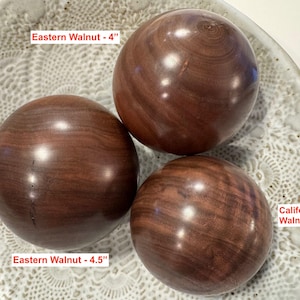 May include: Three smooth, polished wooden spheres with visible grain patterns. The spheres are labeled as Eastern Walnut - 4 inches, Eastern Walnut - 4.5 inches, and California Walnut - 3.75 inches, indicating their specific wood types and diameters.