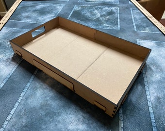 May include: A rectangular, unfinished wooden tray with cut-out handles on the sides. The interior is divided into sections by thin lines. The tray is designed for organizing or displaying items. The tray is sitting on a grey surface.