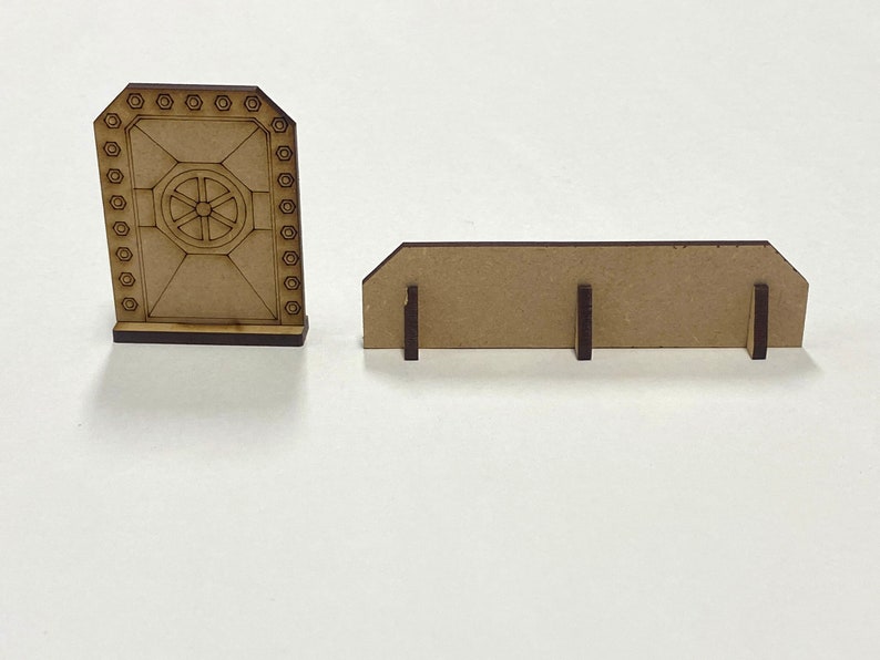 Puede incluir: Dos piezas de madera cortadas con l&aacute;ser. Una es una puerta con un dise&ntilde;o circular en el centro y detalles de pernos hexagonales. La otra es una pieza rectangular con tres patas de soporte. Ambas piezas son de color marr&oacute;n claro.