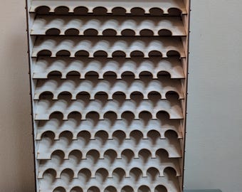 May include: A light-coloured wooden wall-mounted display rack featuring eight horizontal shelves with semi-circular cutouts designed for holding small cylindrical items. The structure has two keyhole slots at the top for mounting purposes.