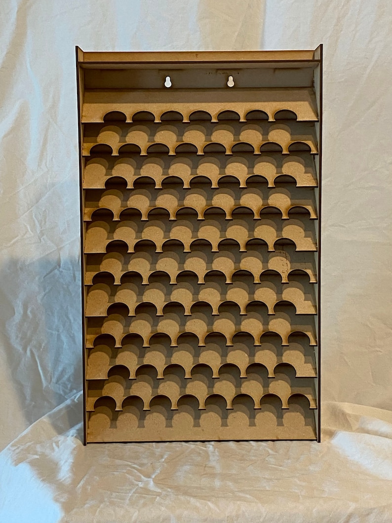 May include: A light brown wooden display shelf featuring numerous semi-circular cutouts for holding small objects. The rectangular shelf has a flat top with two holes for hanging. The design is simple and functional, suitable for displaying collectibles or miniatures.