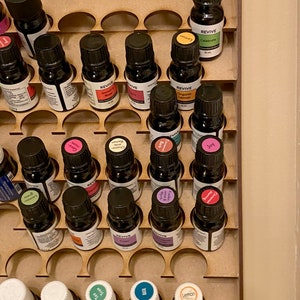 May include: A wooden essential oil organiser filled with small, dark glass bottles. The bottles have black caps and colourful labels, some with the word "REVIVE". The organiser has circular cutouts to hold the bottles securely.
