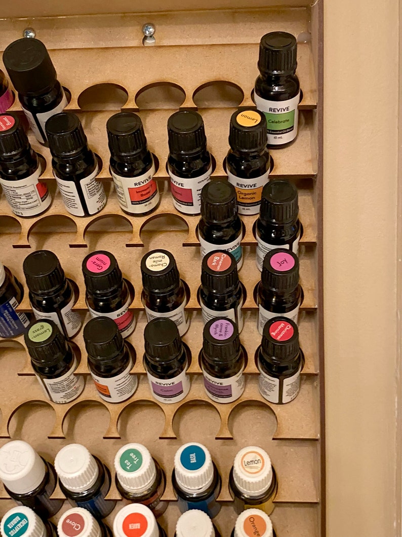 May include: A wooden essential oil organiser filled with small, dark glass bottles. The bottles have black caps and colourful labels, some with the word "REVIVE". The organiser has circular cutouts to hold the bottles securely.