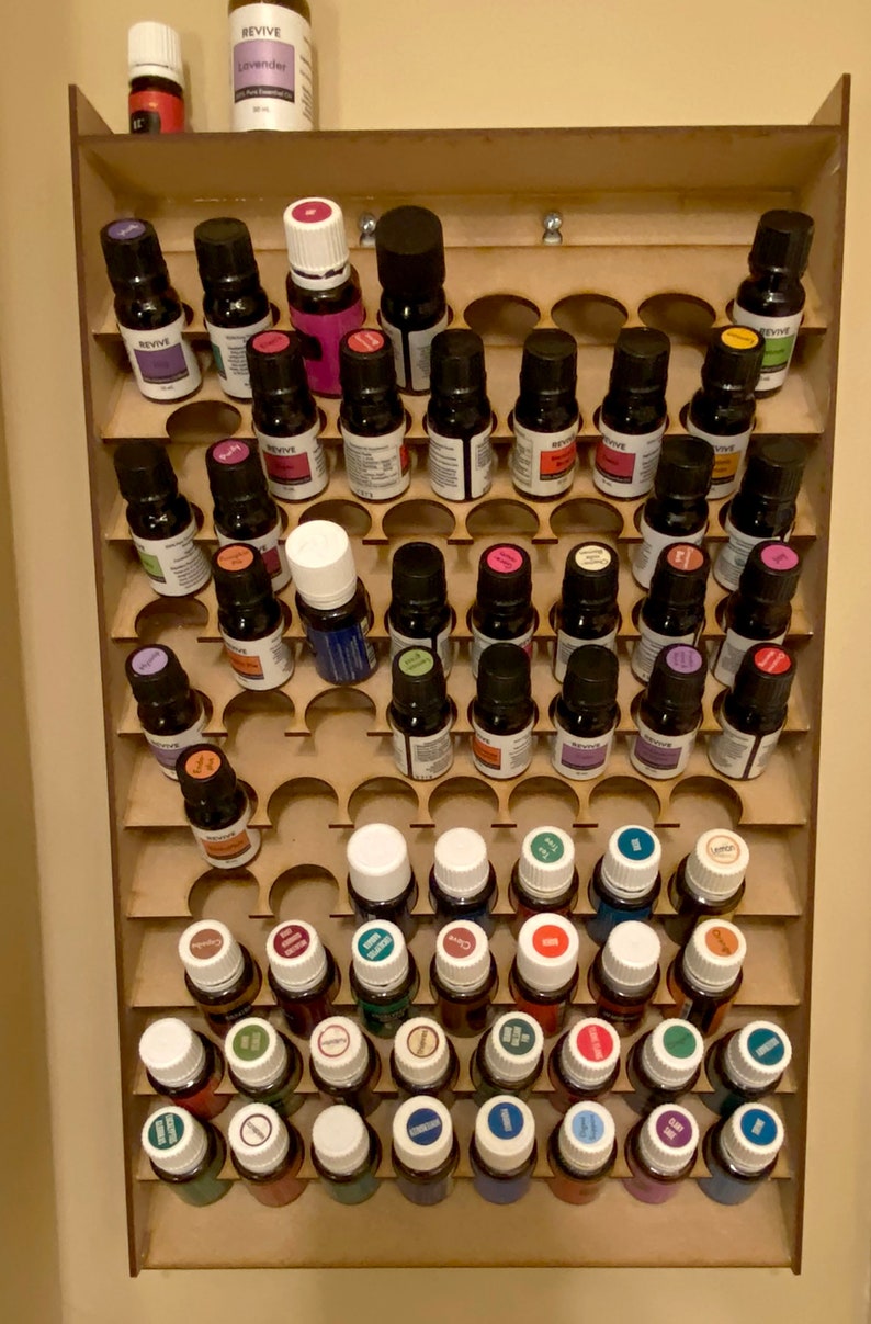 May include: A wooden essential oil organiser filled with numerous small glass bottles. The bottles are arranged in a tiered fashion, showcasing a variety of essential oils. The labels are visible, and the bottles are of different colours.