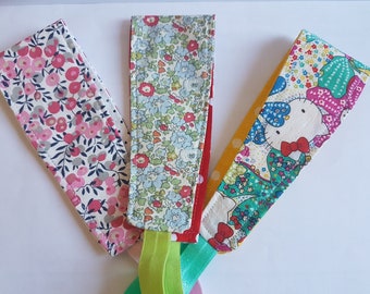 May include: Three fabric headbands with floral and cartoon patterns. The first headband has a pink floral pattern, the second has a blue floral pattern, and the third features a Hello Kitty design. Each headband is attached to a thin elastic band.